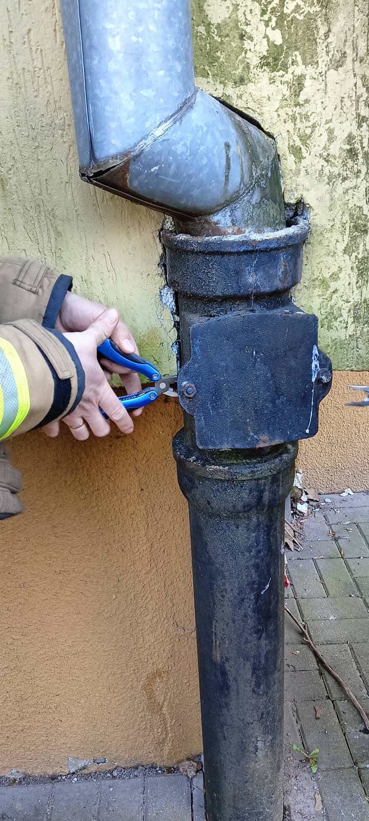 Miejsce w którym utknął ptak. Strażak wykonuje dostęp odkręcając drzwiczki, używając do tego odpowiednich narzędzi.